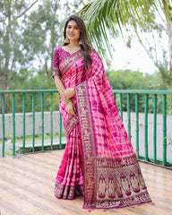 Woman wearing a pink saree with a traditional pattern on a wooden deck with greenery in the background