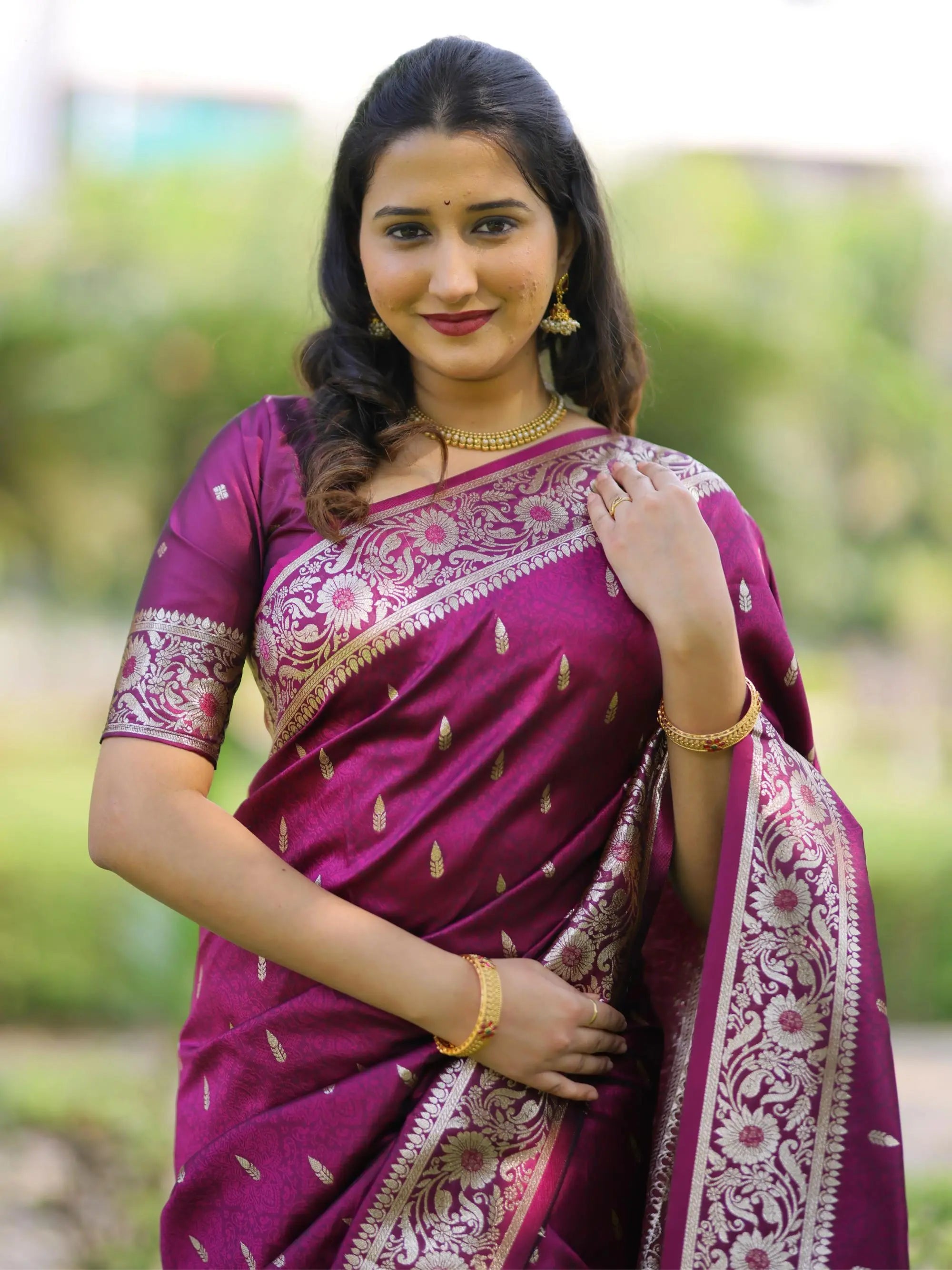 Woman wearing a purple saree with a floral pattern, standing outdoors.