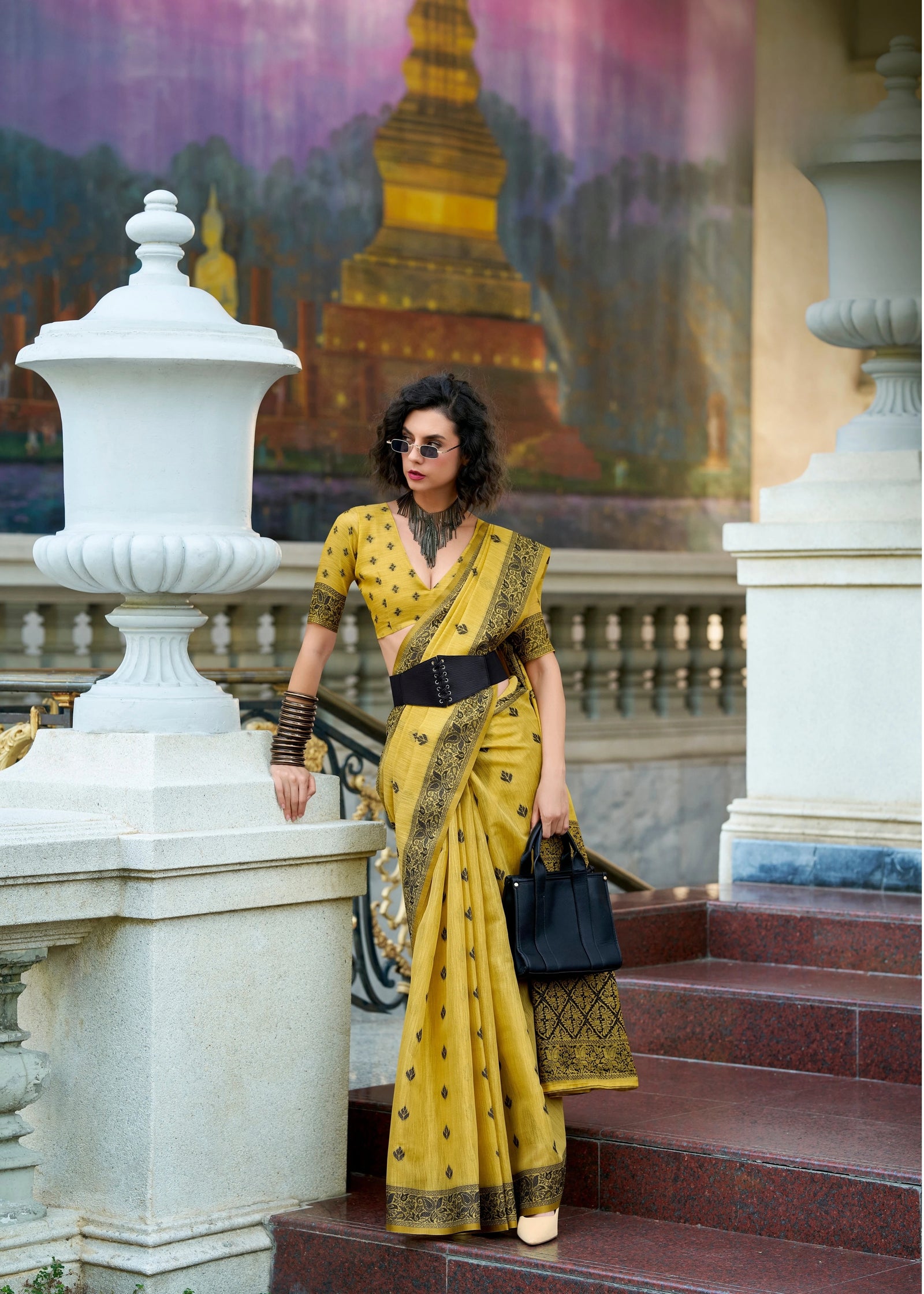 Woman in a yellow saree standing on steps with a colorful mural in the background