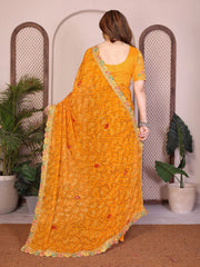 Woman wearing a yellow saree with a pattern, standing in a room with plants.