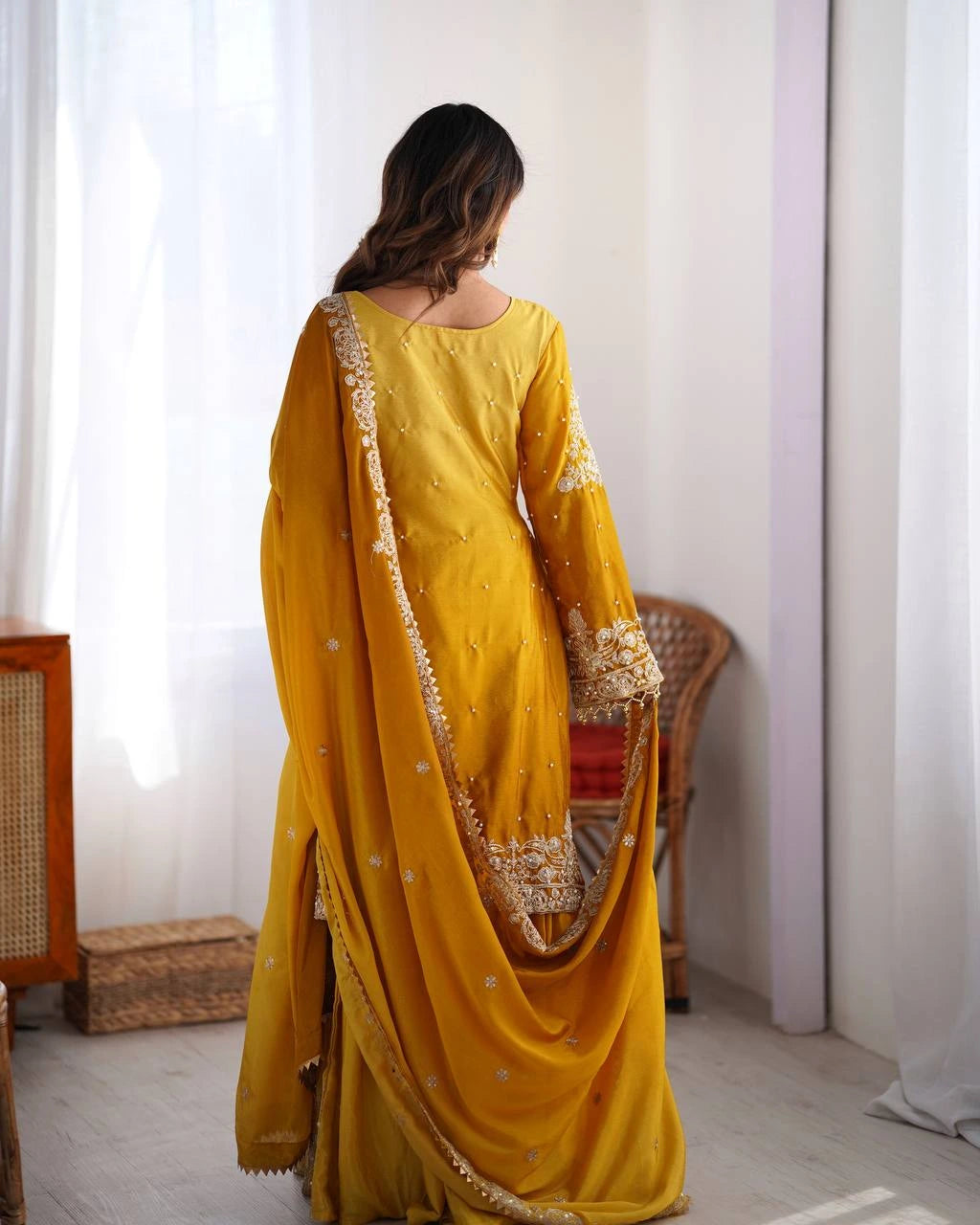 Woman wearing a yellow saree with gold border indoors.