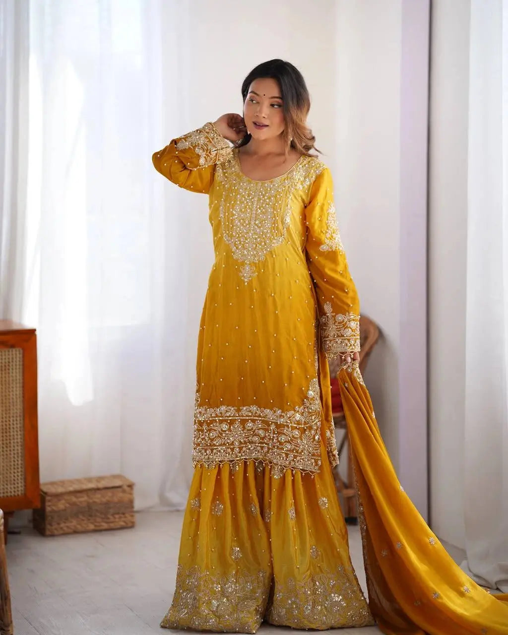 Woman wearing a yellow traditional outfit with gold embroidery in a bright room.