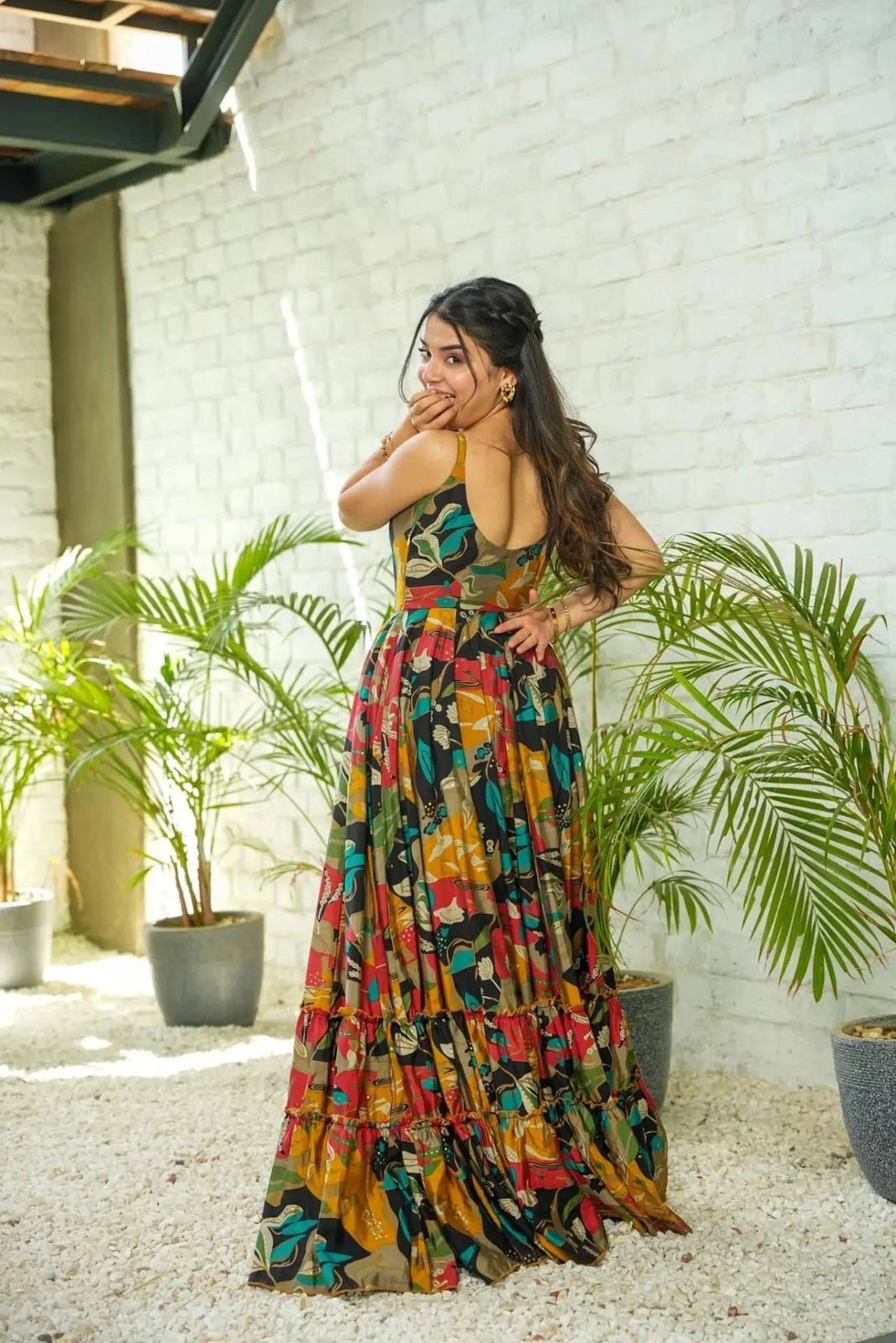 Woman in a colorful dress standing outdoors with plants and a white wall in the background