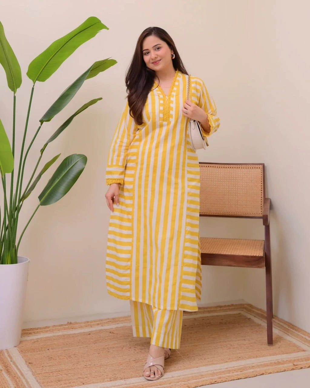 Woman in a yellow and white striped outfit standing next to a plant and chair.