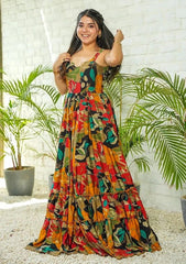 Woman wearing a colorful patterned dress standing in front of a white brick wall with plants.