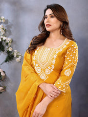 Woman wearing a yellow embroidered dress against a gray background with floral decorations.