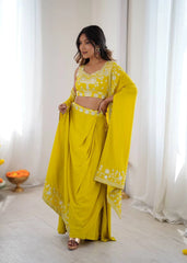 Woman wearing a yellow traditional outfit with white patterns in a bright room.