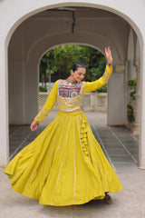 Woman in a yellow traditional outfit with intricate designs standing in an archway.