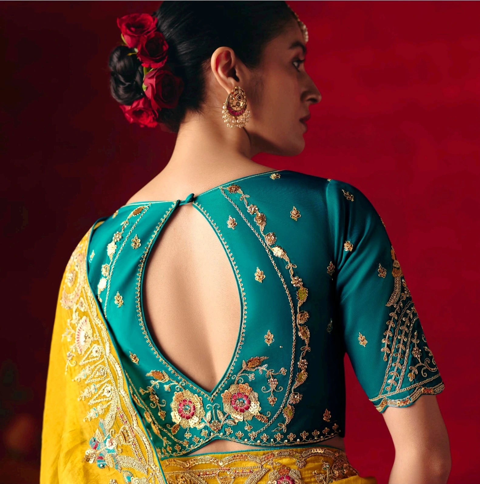 Woman wearing a teal and yellow embroidered blouse with a red background
