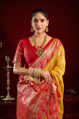 Woman in a red and yellow saree with gold jewelry against a dark background