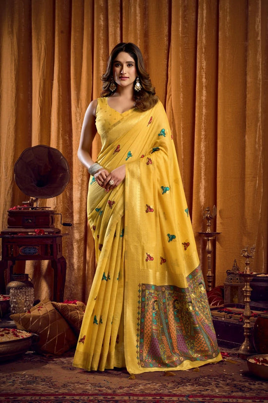 Woman in a yellow saree with butterfly patterns standing against an orange curtain.