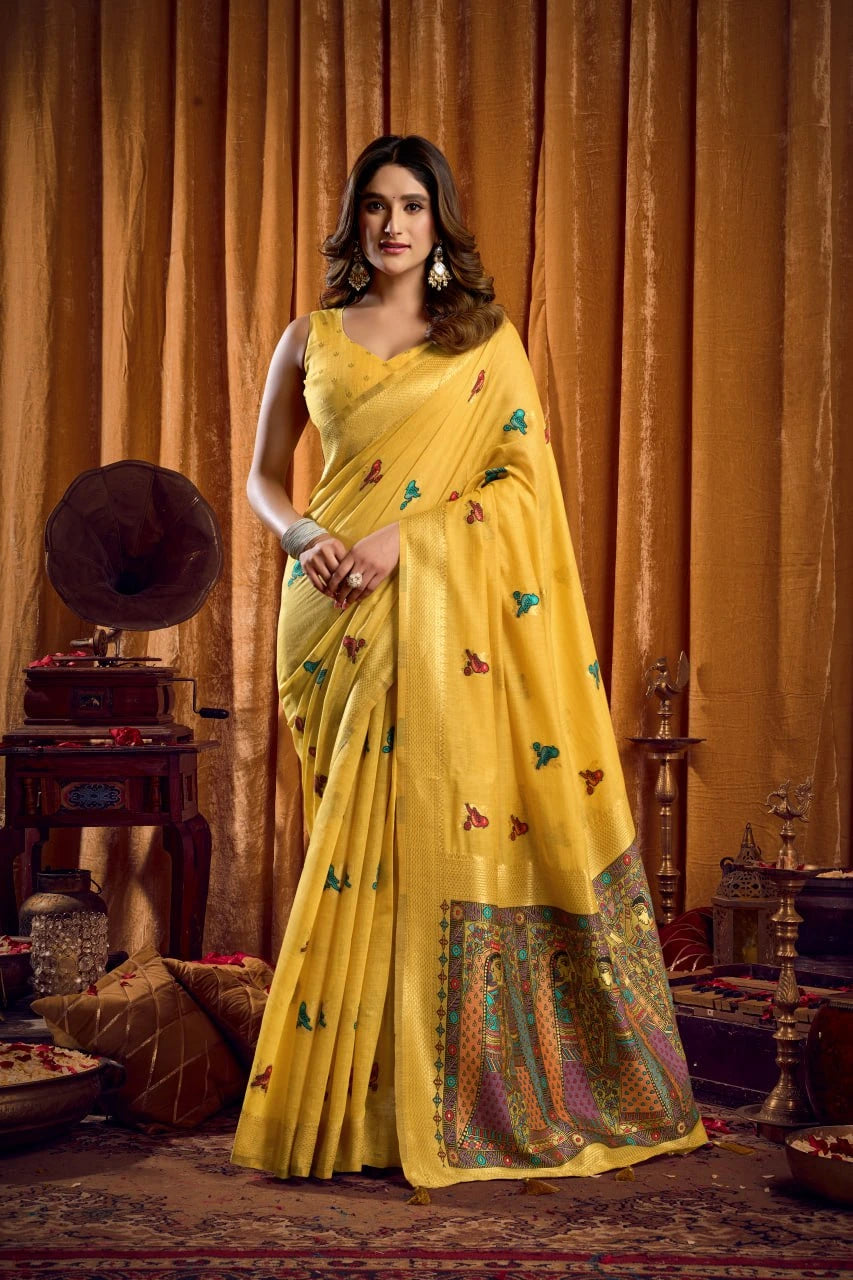 Woman in a yellow saree with butterfly patterns standing against an orange curtain.
