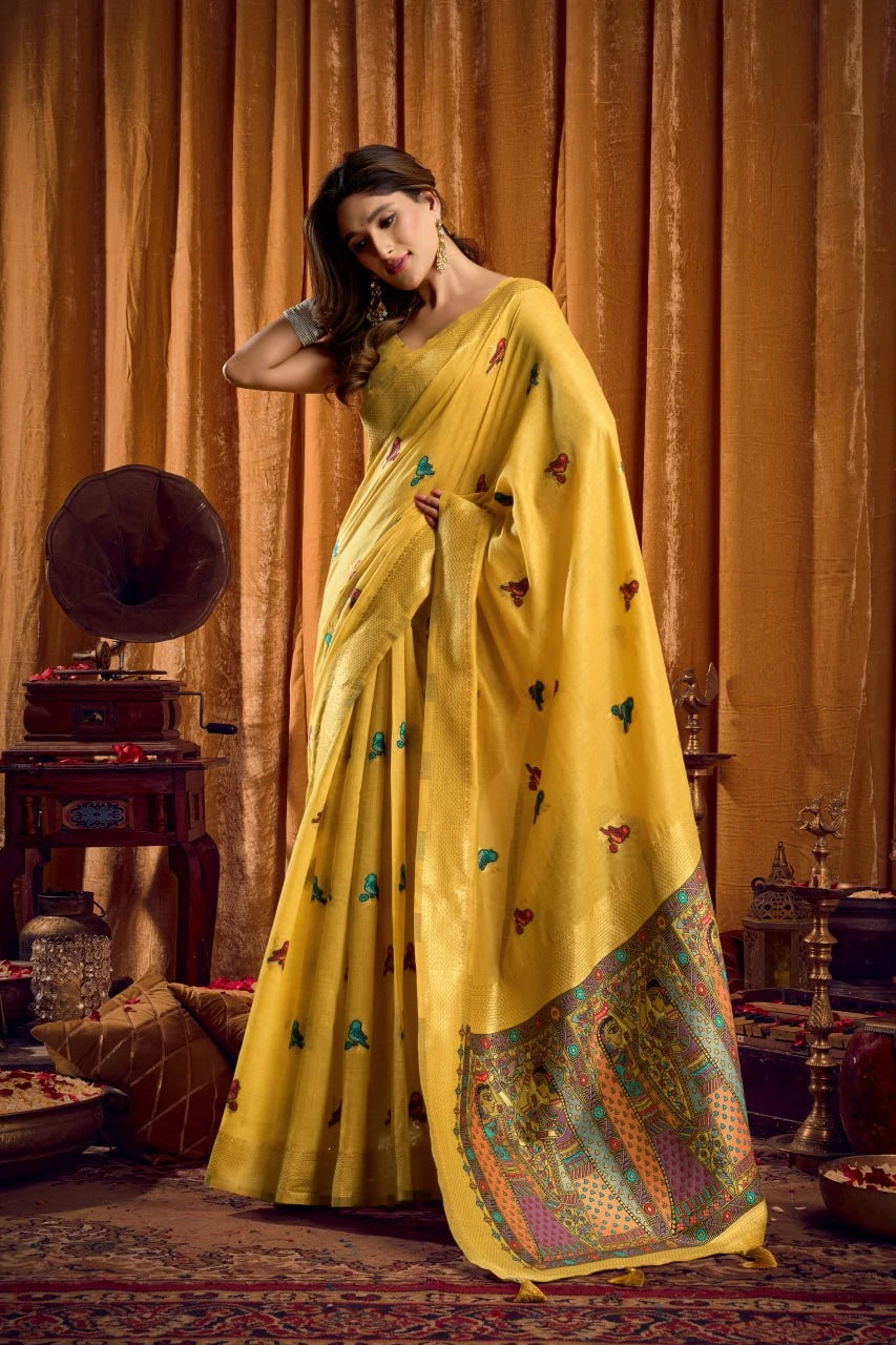 Woman in a yellow saree with intricate patterns standing in a vintage room.