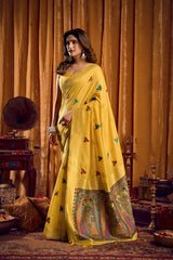 Woman in a yellow saree with intricate patterns standing in a vintage room.
