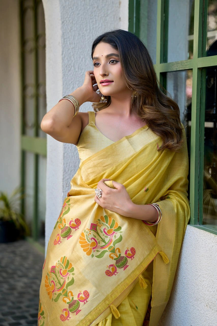 Woman in a yellow saree with floral patterns leaning against a wall.