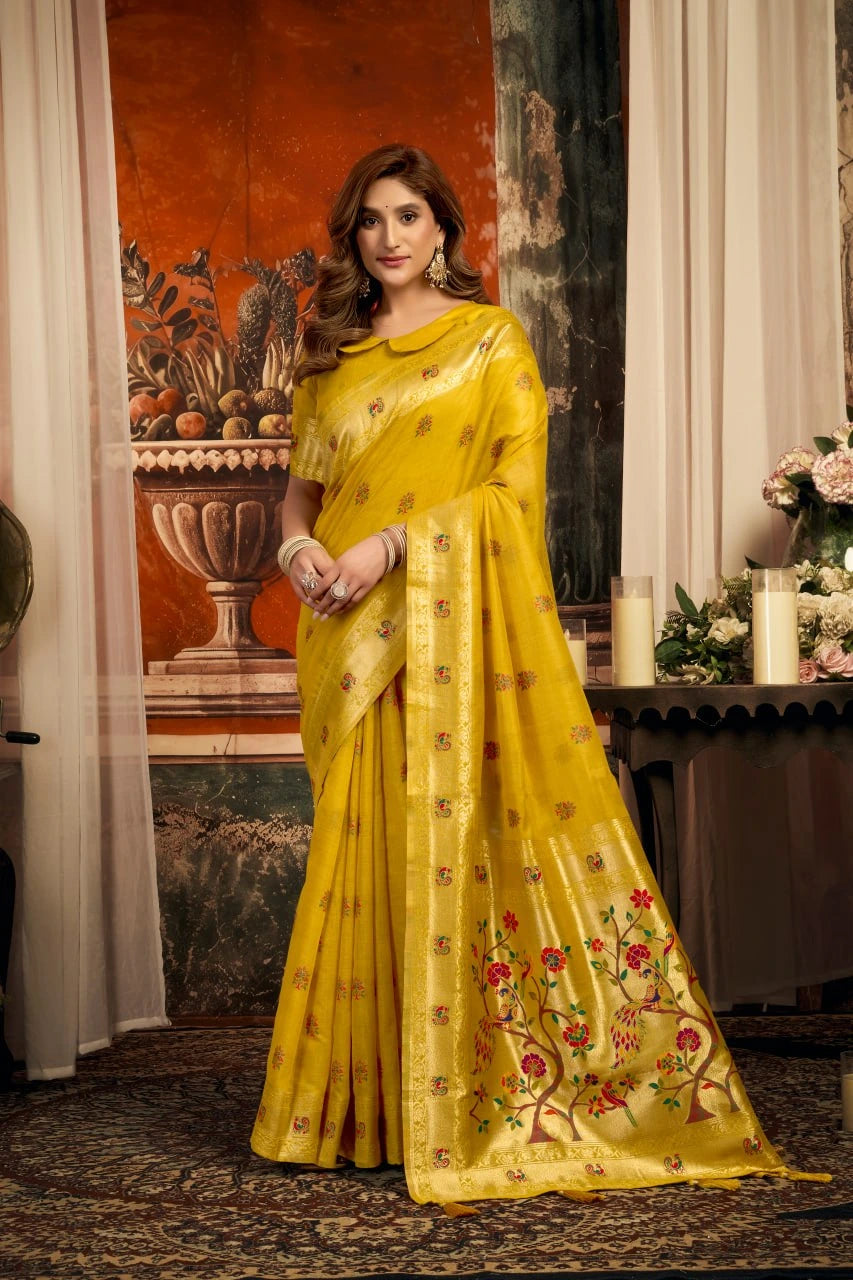 Woman in a yellow saree with floral patterns standing in an elegant room.
