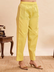 Yellow straight-fit pants with elastic waistband, paired with transparent heeled sandals, styled against a neutral background with a vintage side table.