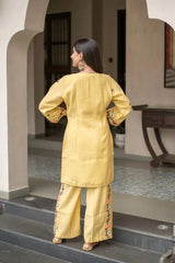 Woman in a yellow traditional outfit standing on steps with a neutral background