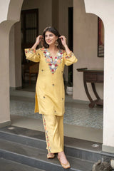 Woman in a yellow embroidered outfit standing on steps inside a building.