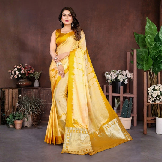 Woman in a yellow saree standing in a room with plants and flowers.