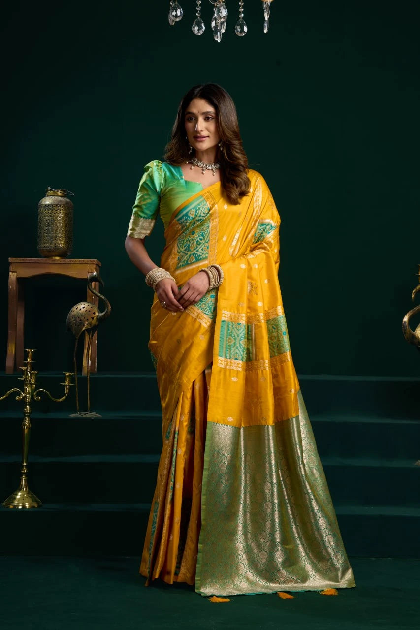 Woman in a yellow and green saree standing in a dark room with decorative elements.