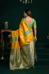 Woman in a yellow and green saree standing in a dimly lit room.