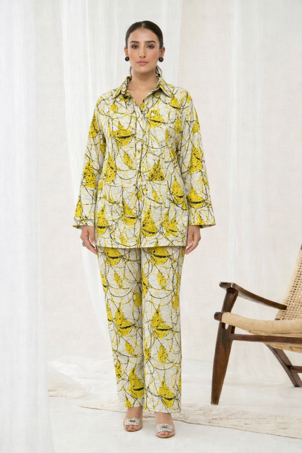 Woman wearing a yellow and green patterned outfit standing in a room with a chair.