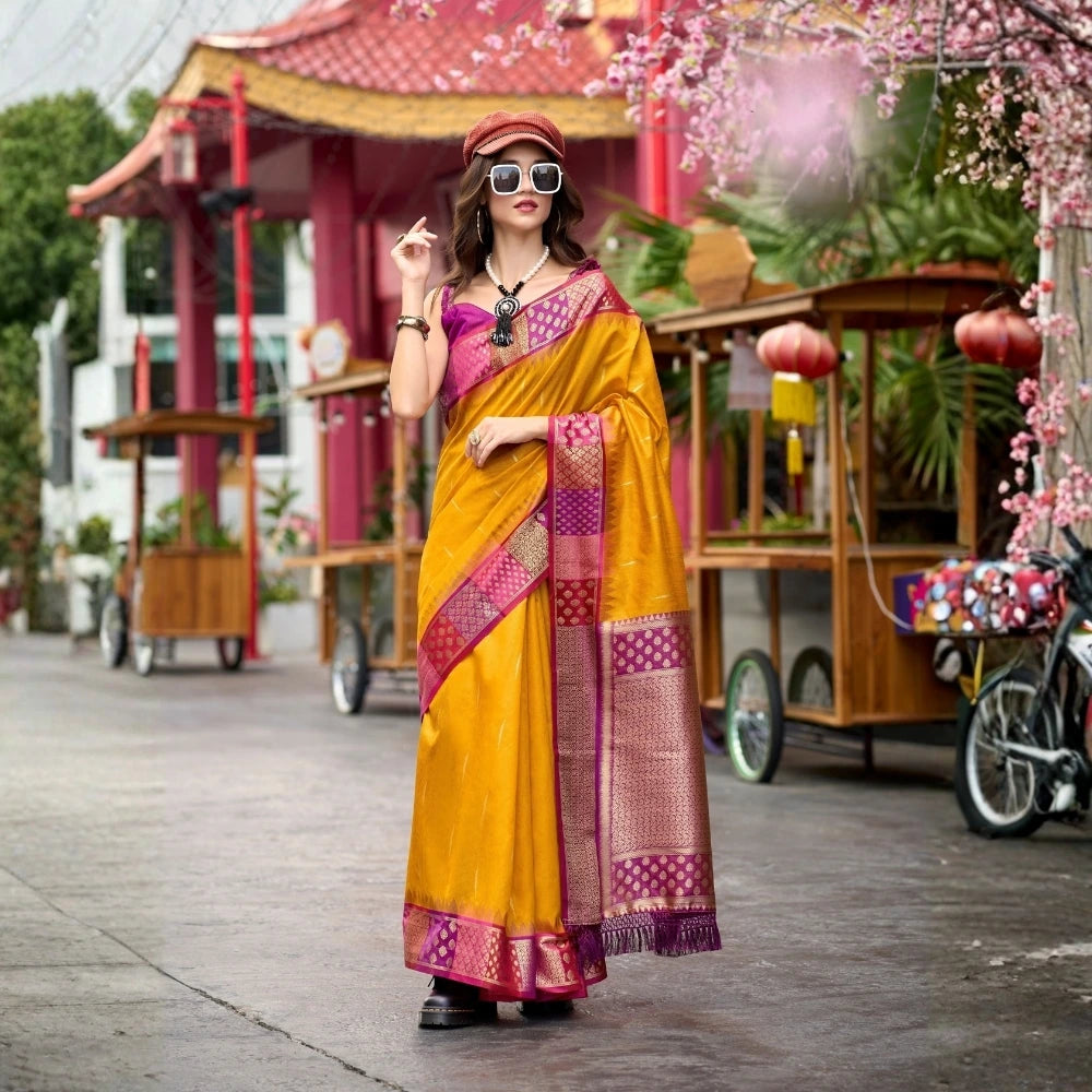 Woman in a yellow saree with pink blouse standing in front of traditional wooden carts.