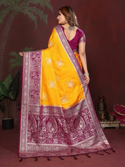 Woman wearing a yellow and purple saree with a patterned border against a dark background