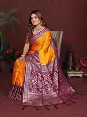 Woman in a traditional orange and purple saree sitting on a chair with a dark background