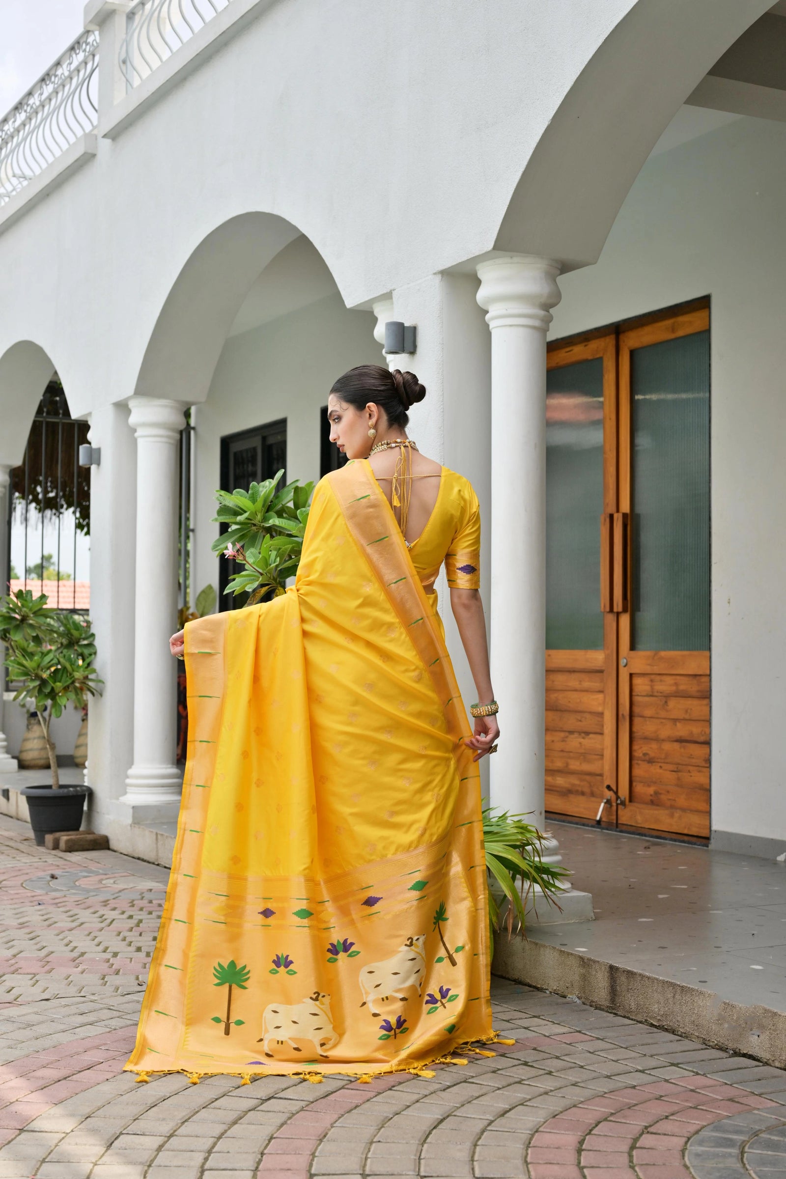 Woman in a yellow saree standing in front of a white archway with wooden doors.