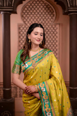 Woman in a yellow saree with green border standing in front of an ornate archway.