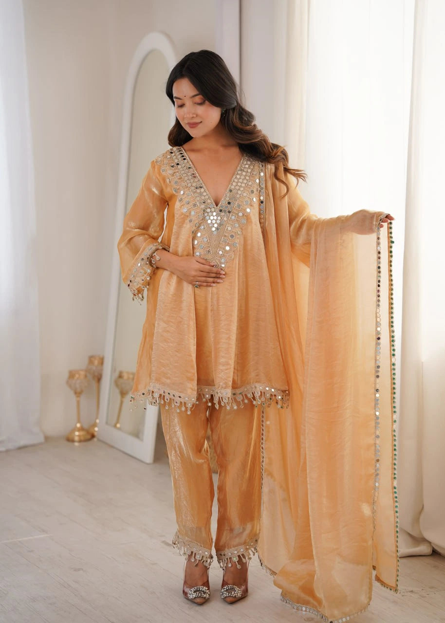 Woman in a peach embroidered outfit standing in a softly lit room.