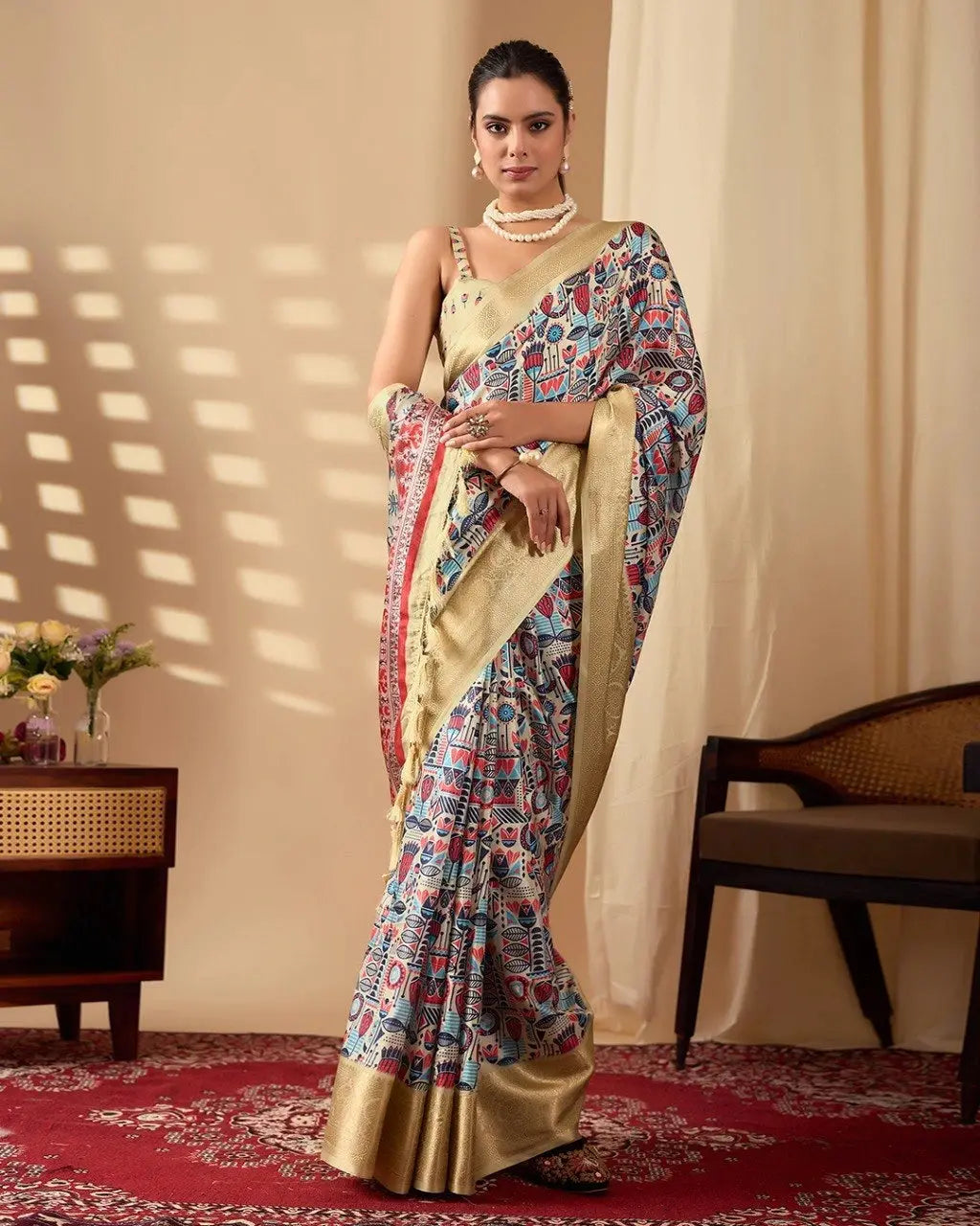 A woman wearing a cream saree with colorful folk-inspired prints and a rich golden woven border, paired with elegant pearl jewelry.