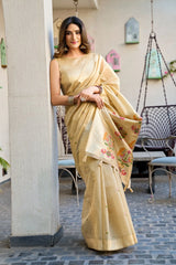 Woman in a beige saree with floral patterns standing indoors.