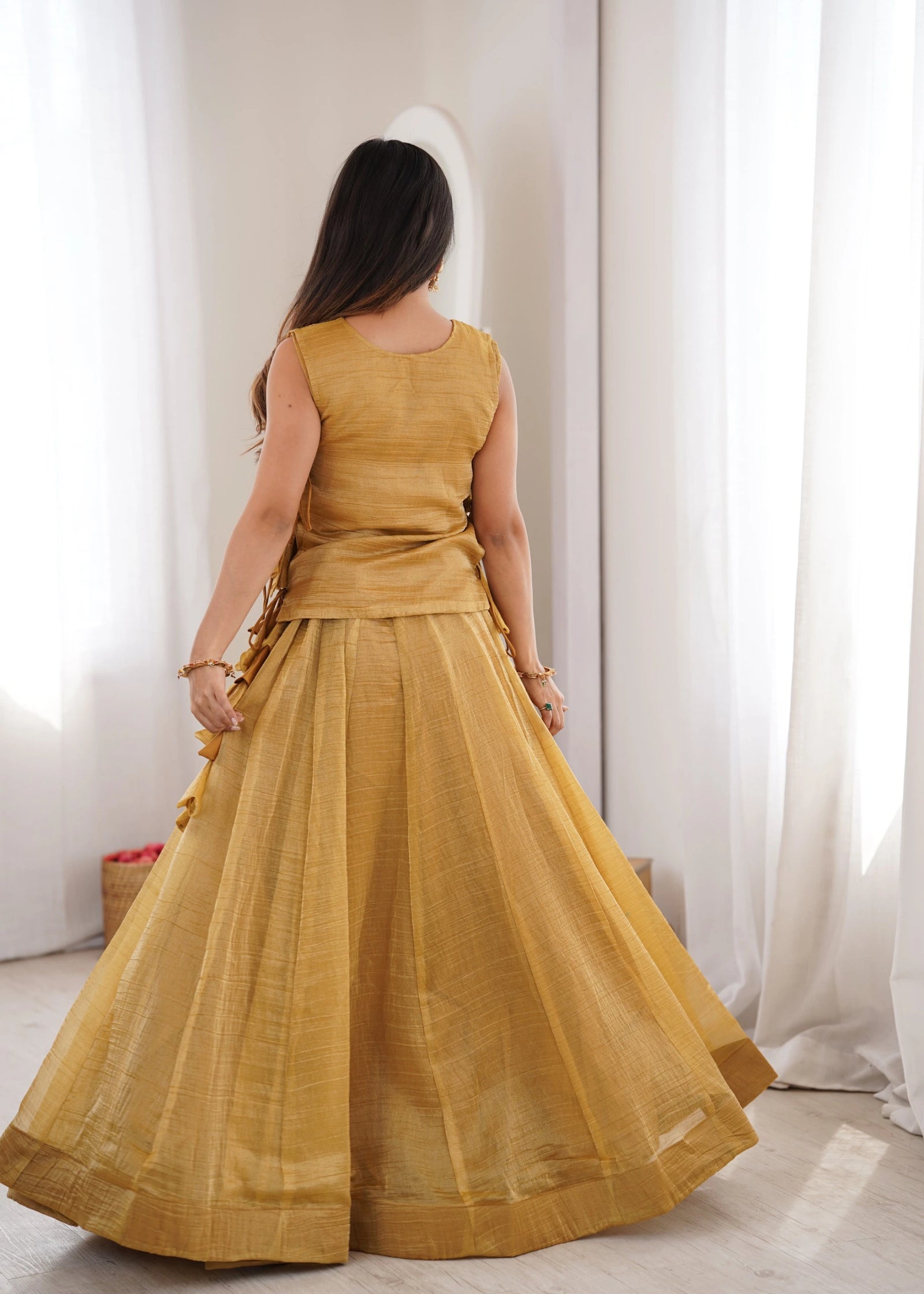 Woman wearing a mustard yellow dress standing in a room with white curtains.