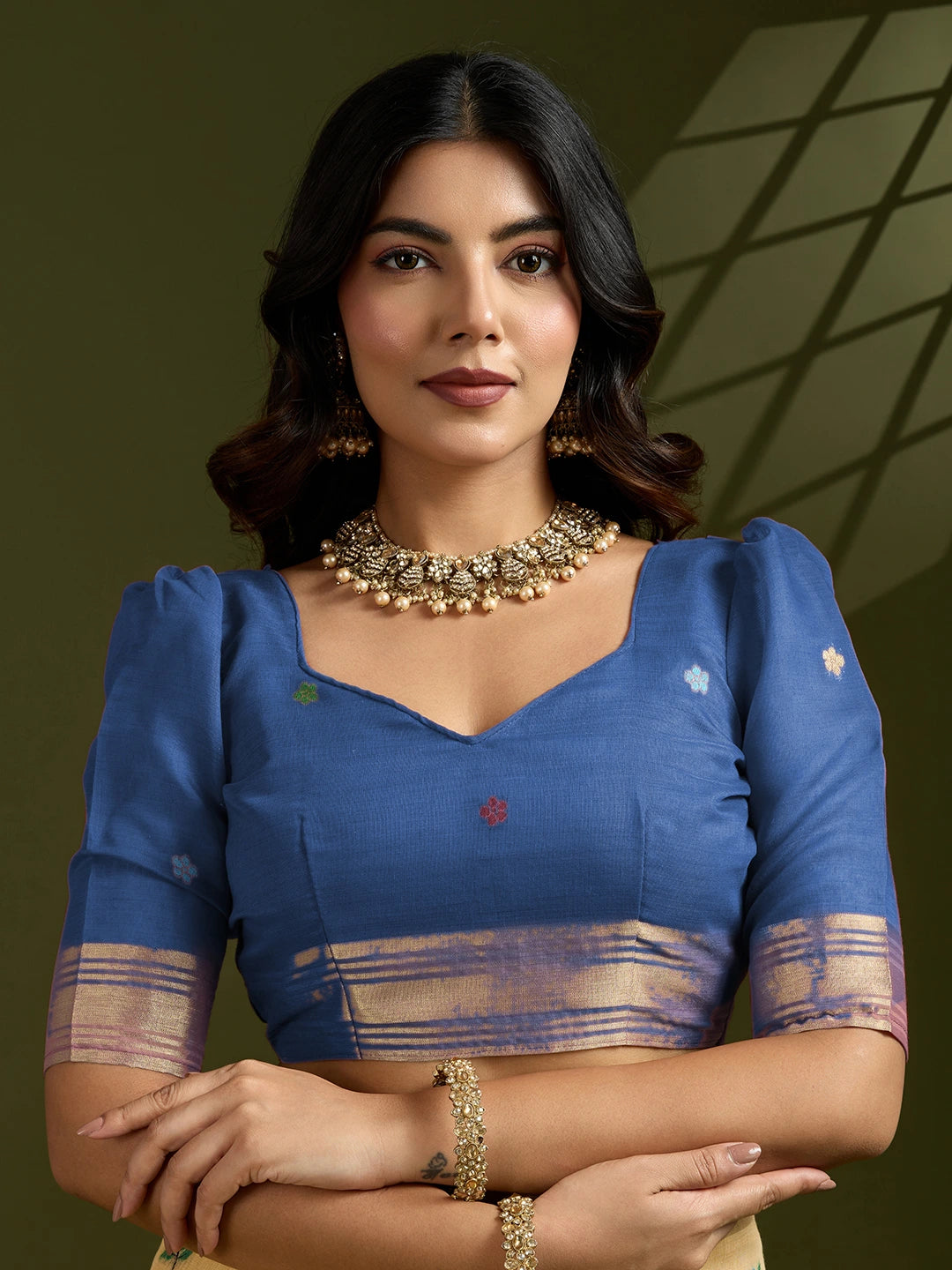 Woman wearing a blue traditional outfit with gold jewelry against a green background