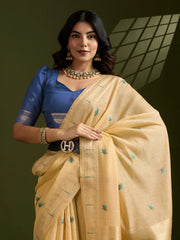 Woman wearing a blue blouse and beige saree with green patterns against a dark background