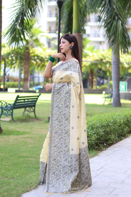 Woman wearing beige traditional weaving saree posing elegantly in lush green outdoor setting