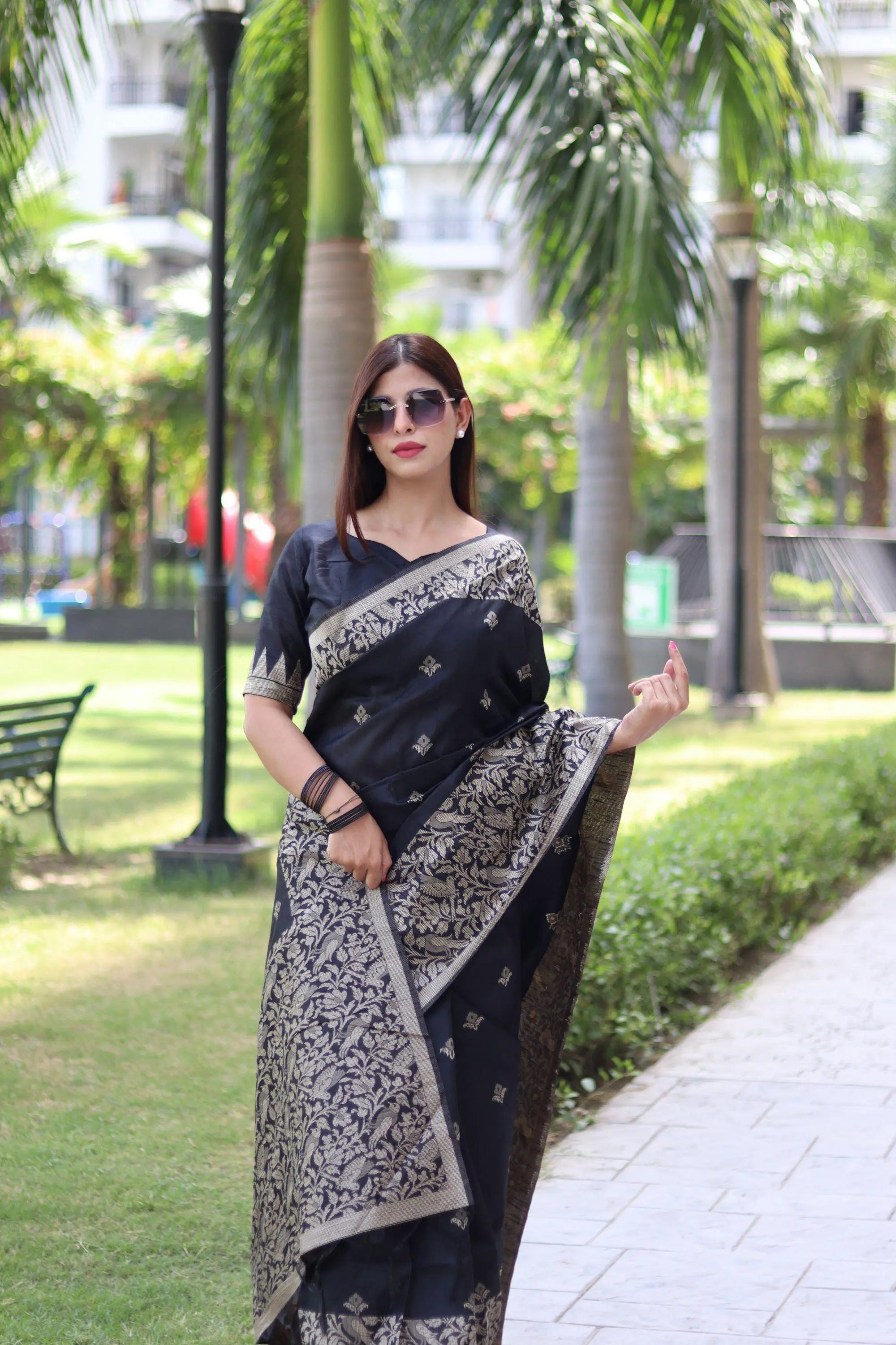 Woman in elegant black traditional weaving saree posing confidently in garden setting