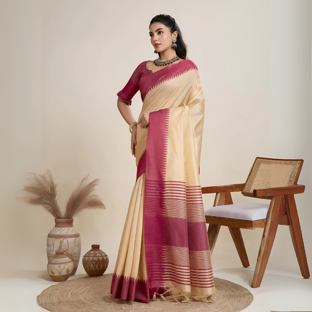 A woman models a striking Beige Raw Silk Saree. The saree has a wide, vibrant deep pink border featuring traditional temple weaving. The pallu has wide horizontal stripes in pink and gold. She wears a pink blouse and a gold and green Kundan necklace.