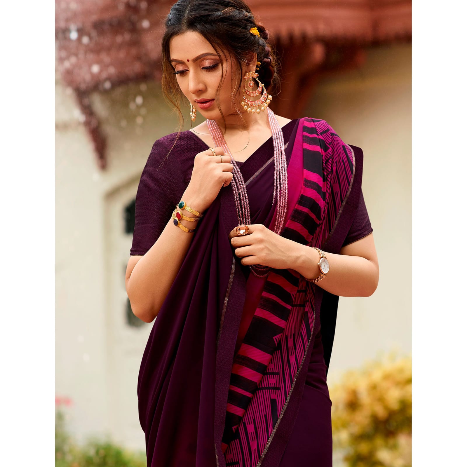 Woman in a deep shade purple jacquard work saree with gold border standing indoors in an elegant room with arched decor and vintage furniture elements