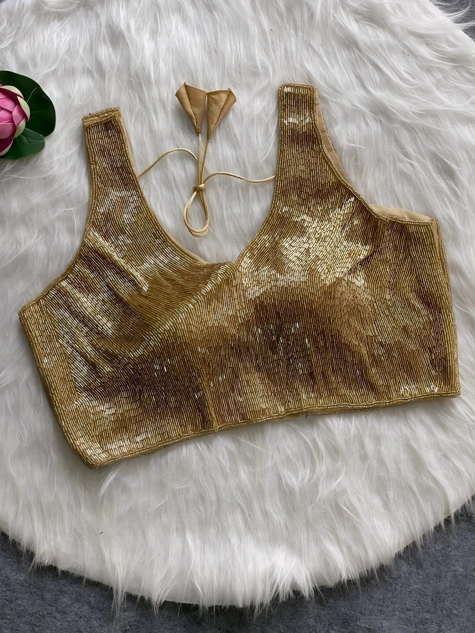 Gold sequin sleeveless blouse with tie-back detail, displayed on a white fur background with a pink floral prop