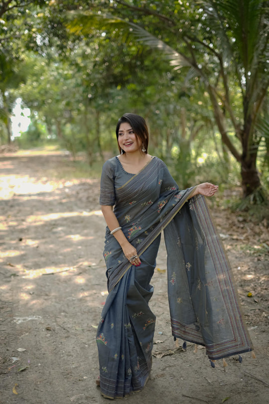 Woman wearing gray traditional weaving saree with intricate design in a lush garden background