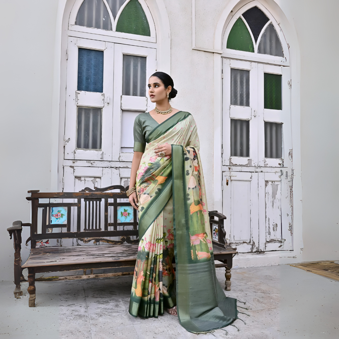 A woman models an elegant Off-White Soft Silk Saree featuring a large-scale, colorful floral and foliage Pichwai-style print. The saree has a wide Dark Olive Green border and pallu. She wears a matching short-sleeve green blouse and a gold Kundan choker necklace, posing outdoors next to antique white doors.