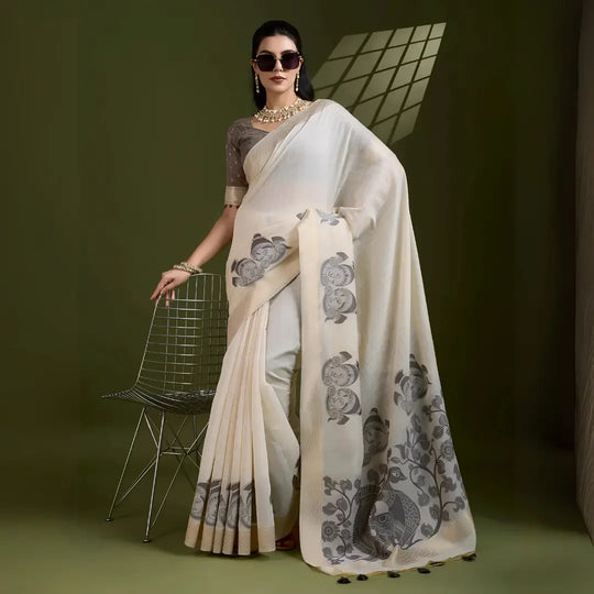 A woman models an elegant Beige Soft Muga Cotton Saree. The saree features large Kalamkari-style prints of peacocks, trees, and florals in a contrasting Dark Gray on the pallu. She wears a dark gray short-sleeve sheer blouse and accessorizes with a gold Kundan choker necklace and sunglasses.