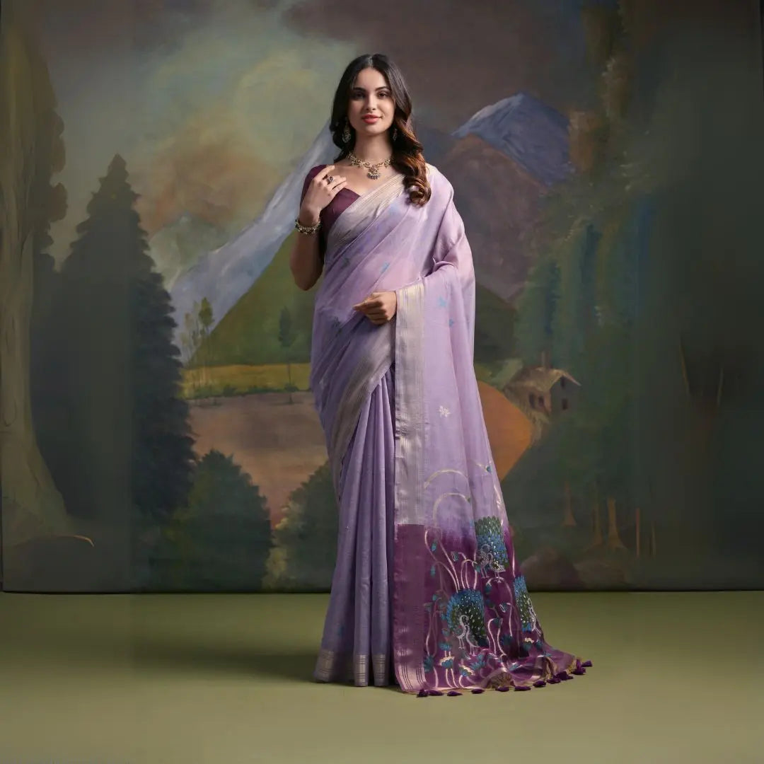 A woman models a soft Lavender Muga Silk Saree with subtle Resham weaving. The pallu dramatically transitions to a deep purple color, featuring intricate blue and purple peacock Resham threadwork. She wears a dark purple blouse and a gold Kundan necklace.