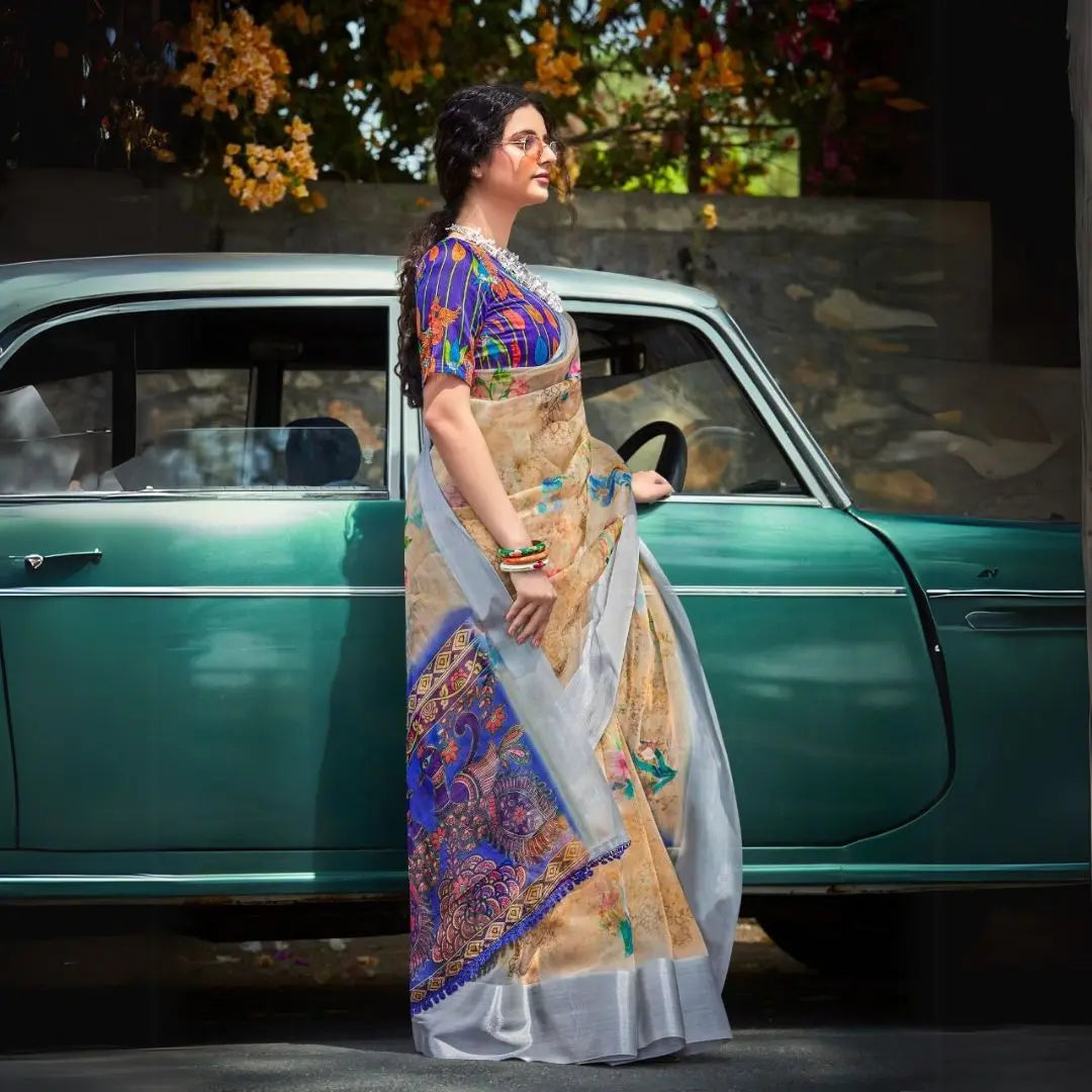 Woman in a light beige floral print saree standing beside a vintage car with colorful flowers in the background