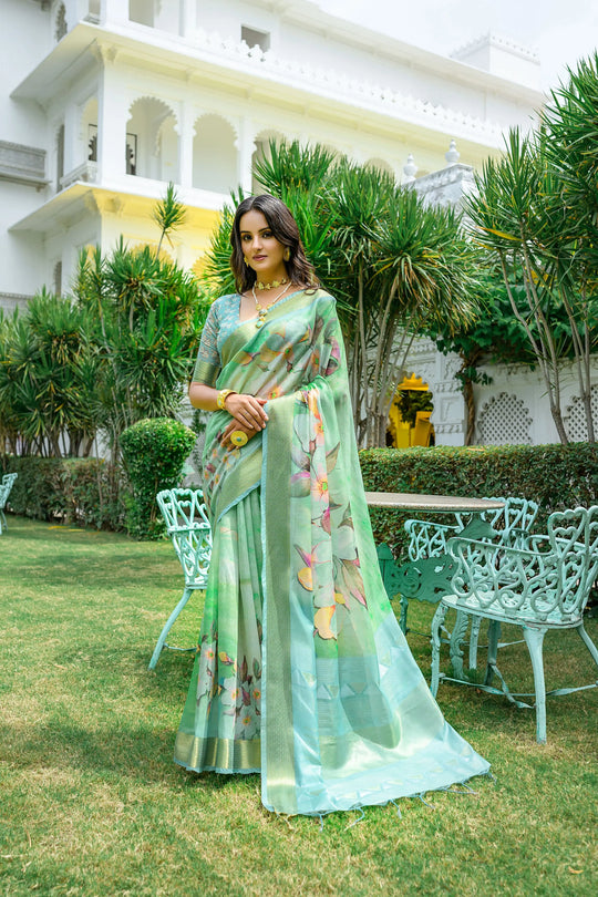 Woman wearing light green pastel saree with zari work and floral design in a luxurious garden setting
