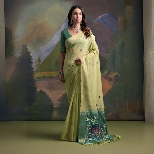 A woman models a soft Pista Green Muga Silk Saree with subtle Resham weaving. The pallu dramatically transitions to a deep teal color, featuring intricate purple and green floral/peacock Resham threadwork. She wears a teal blouse and an oxidized silver necklace.